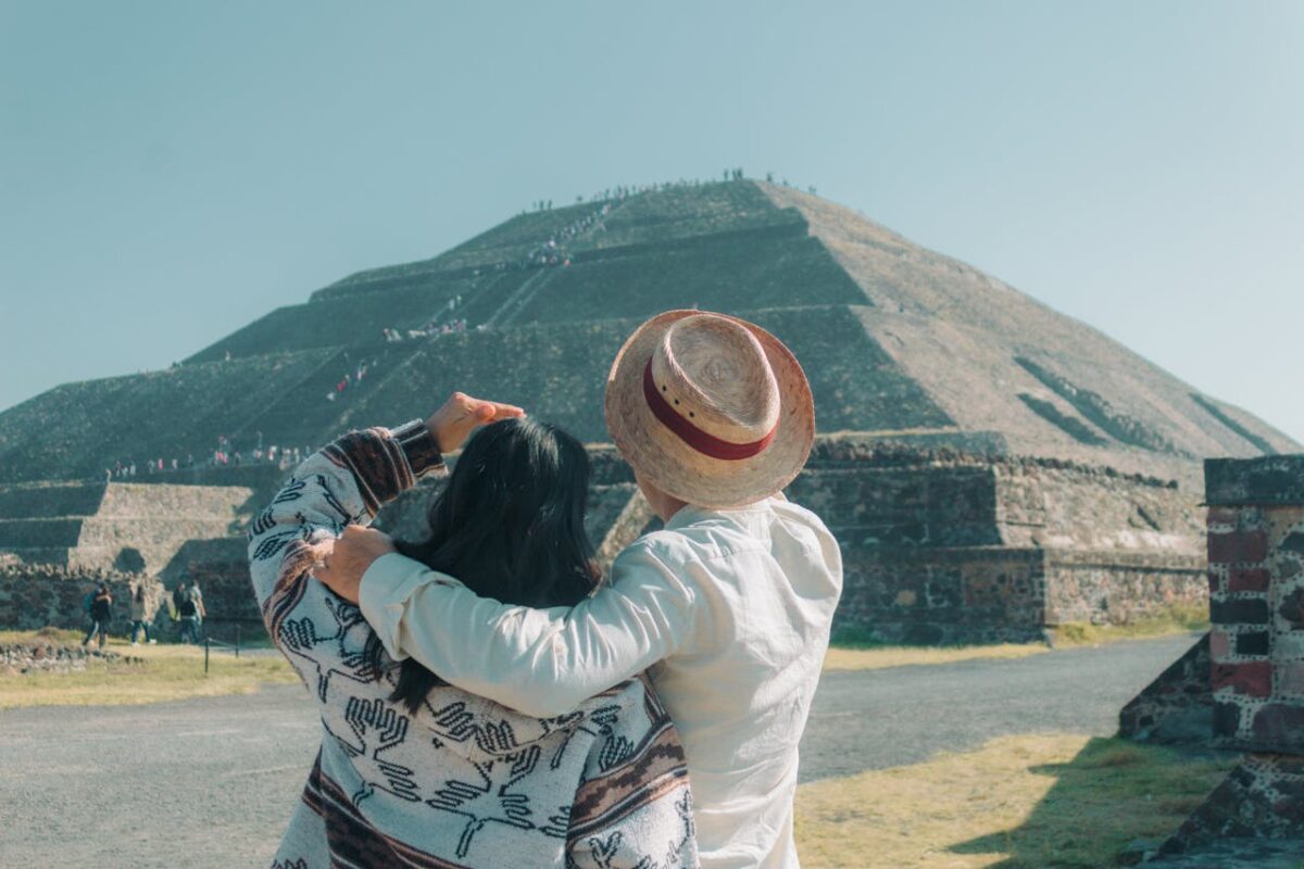 A couple embraces while admiring the Pyramid of the Sun in Teotihuacan under a clear sky.