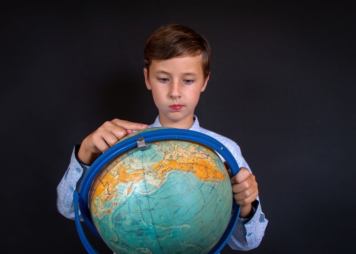 A young boy in a shirt examines a globe against a black background, reflecting study and curiosity.